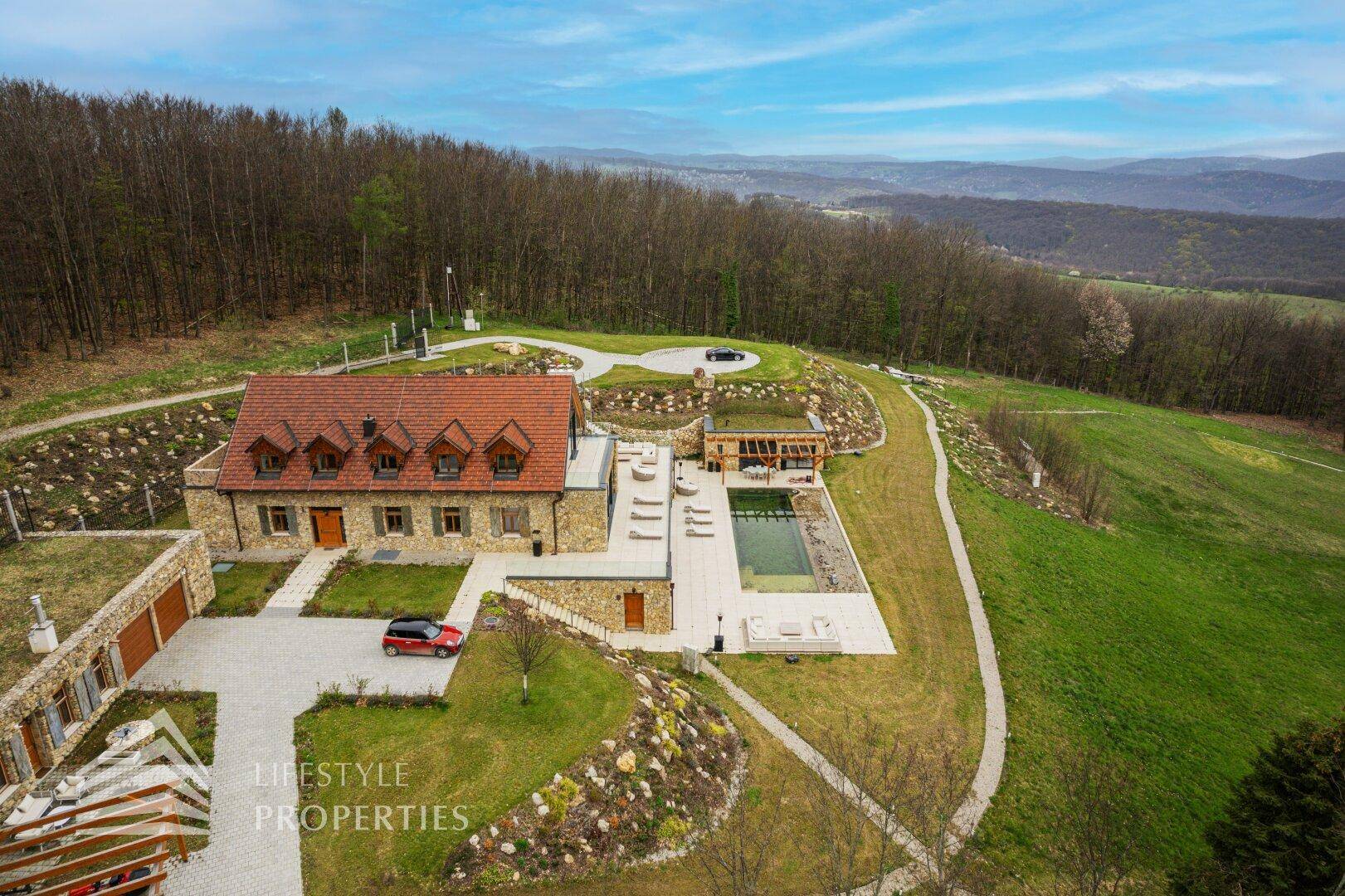 Luftaufnahme des Anwesens mit traditionellem und modernem Gebäudeteil, Pool und weitläufiger Landschaft.