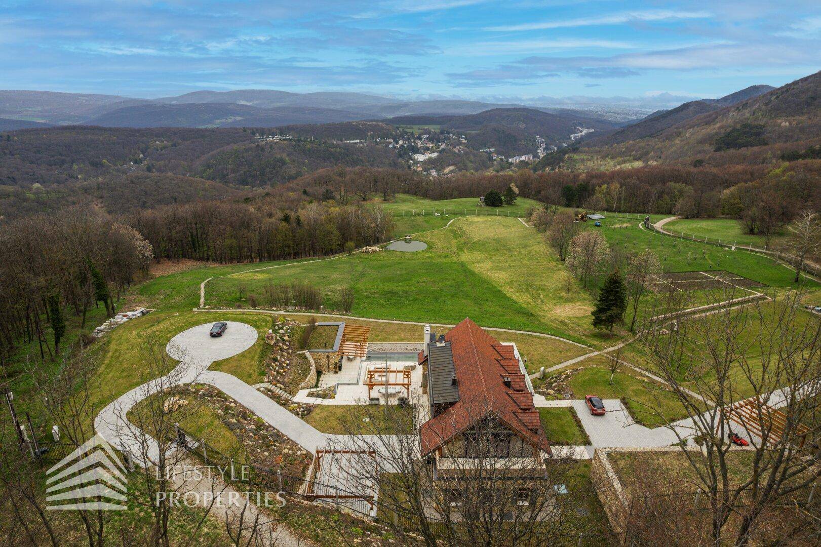 Luftaufnahme des Anwesens in einer Talmulde mit Blick auf die umliegenden Berge und Wälder.