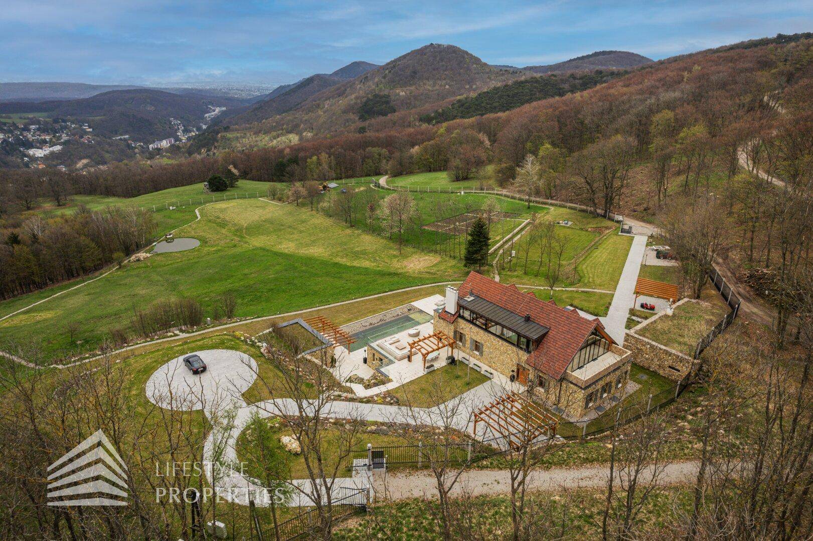 Panoramische Luftaufnahme des Anwesens mit Zufahrtswegen und beeindruckendem Bergpanorama.