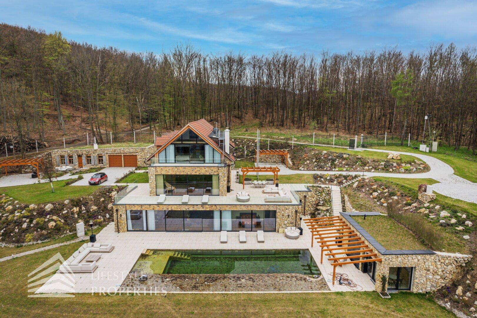 Detailansicht des modernen Hauses mit großzügigem Poolbereich, Sonnenterrassen und grüner Umgebung.