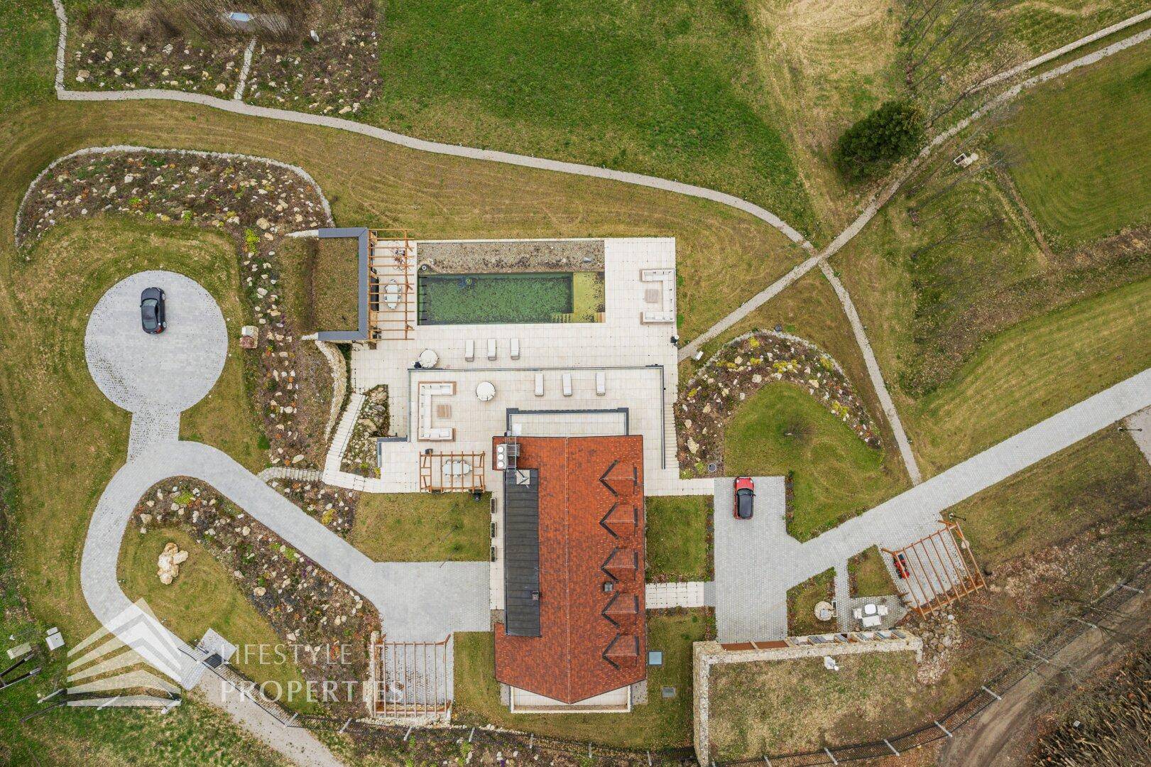 Vogelperspektive des Anwesens mit Hauptgebäude, Pool, Zufahrten und umgebender Naturlandschaft.