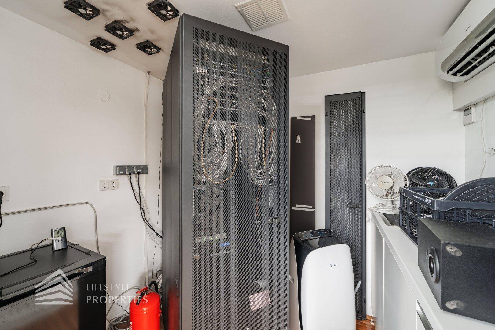Technikraum mit Server-Rack, Klimaanlage und Lüftern an der Decke für optimale Kühlung.