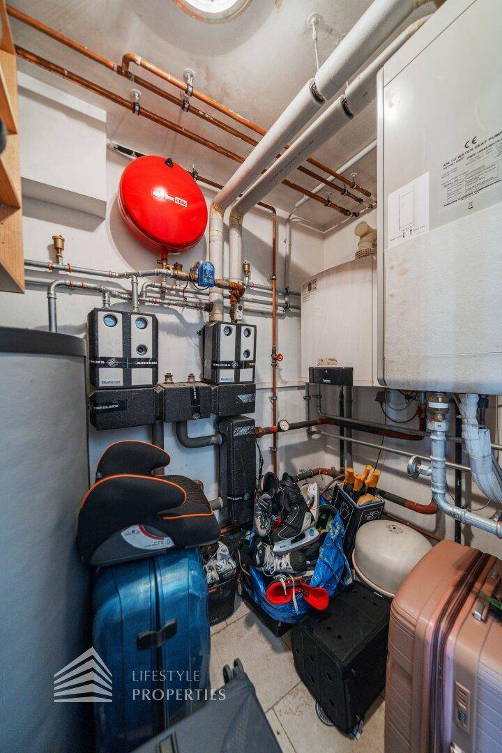 Technikraum mit Heizungsanlage, Rohren und verschiedenen Geräten, auch als Abstellraum genutzt.