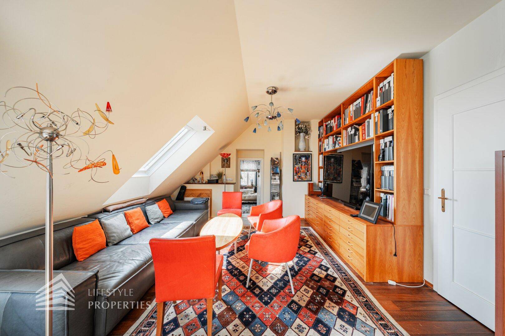 Gemütlicher Dachgeschoss-Wohnbereich mit Schrägen, Dachfenster, Bücherregalen und einem Fernseher.
