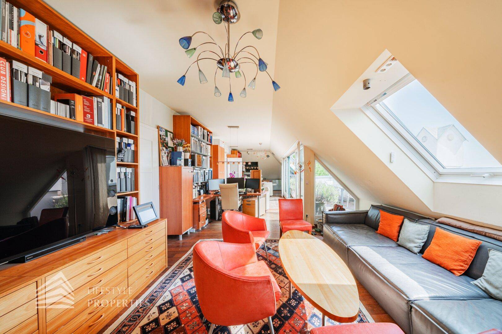 Geräumiger Dachgeschoss-Wohnbereich mit umfangreichen Bücherregalen, Fernseher und viel Tageslicht.