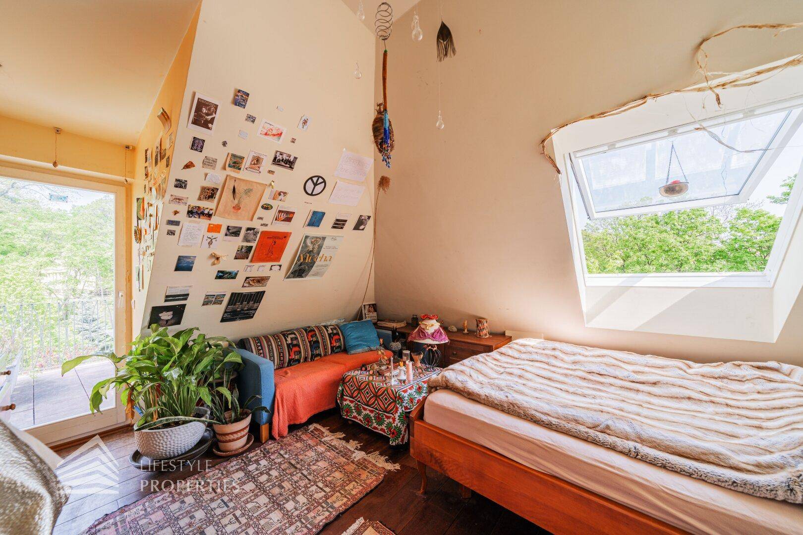 Dachgeschoss-Schlafzimmer mit Dachfenster, Holzboden und Balkonzugang.