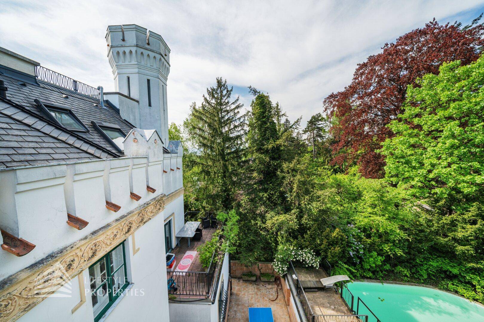 Historisches Gebäude mit Turm und Blick auf den Gartenbereich mit Pool und üppiger Vegetation.