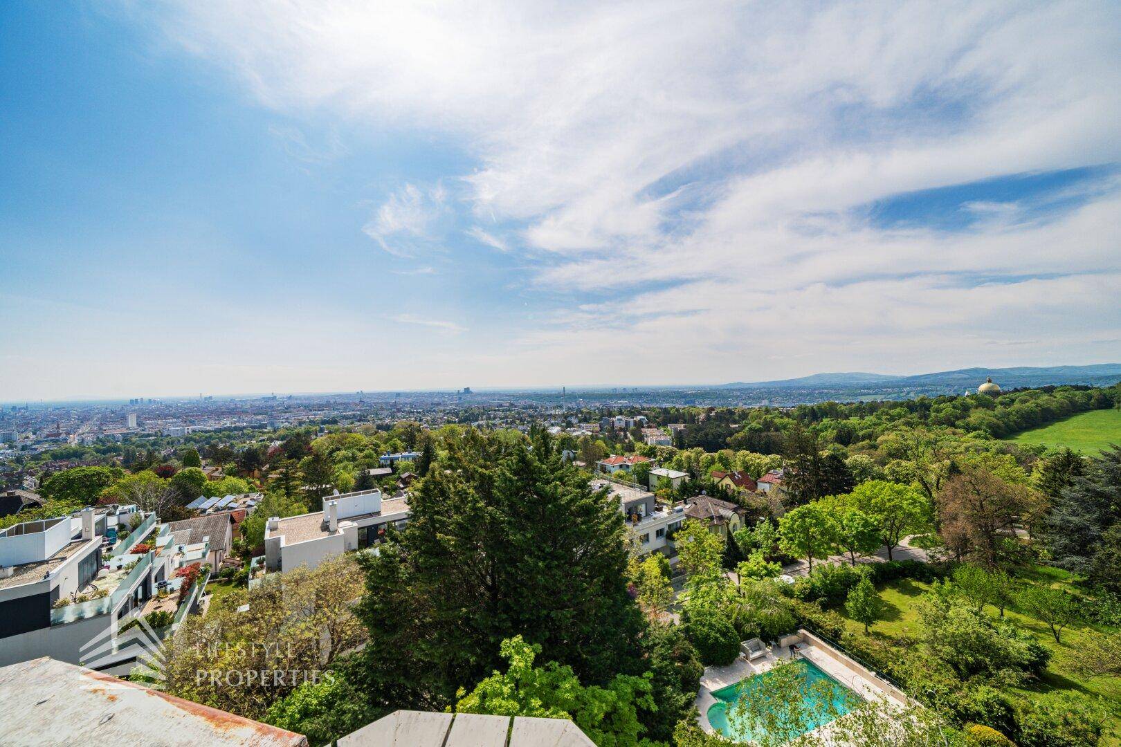 Weitläufiger Blick über die Stadt und die grüne Umgebung mit einem sichtbaren Poolbereich.