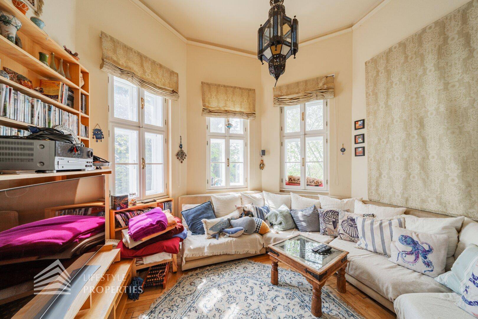 Gemütlicher Erkerraum mit Ecksofa, vielen Fenstern und einer orientalisch anmutenden Hängelampe.
