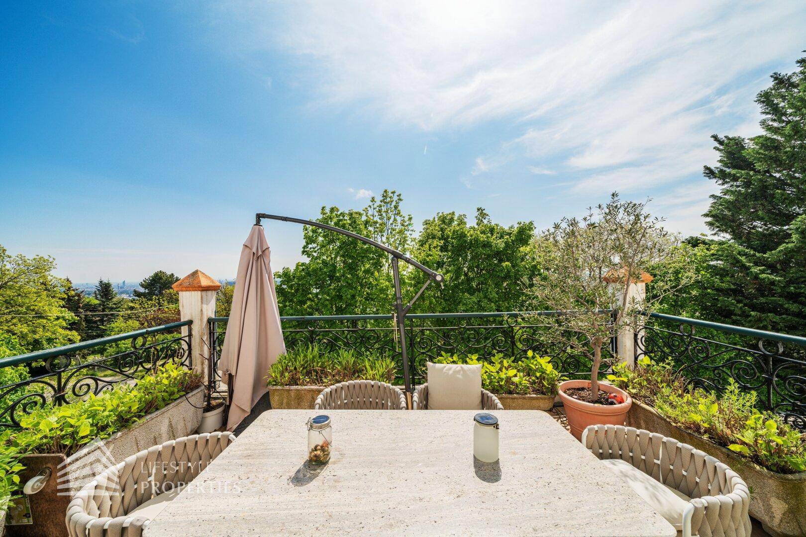 Heller Balkon mit Esstisch, Sonnenschirm und Blick auf die grüne Umgebung.