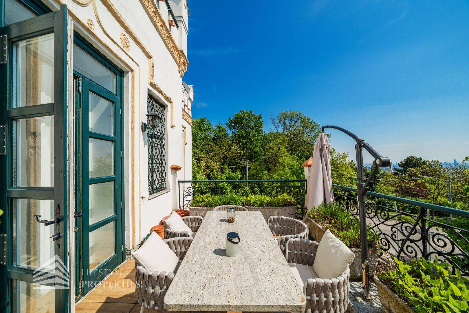 Eleganter Balkon mit Esstisch und Zugang zum Innenbereich, umgeben von üppigem Grün.