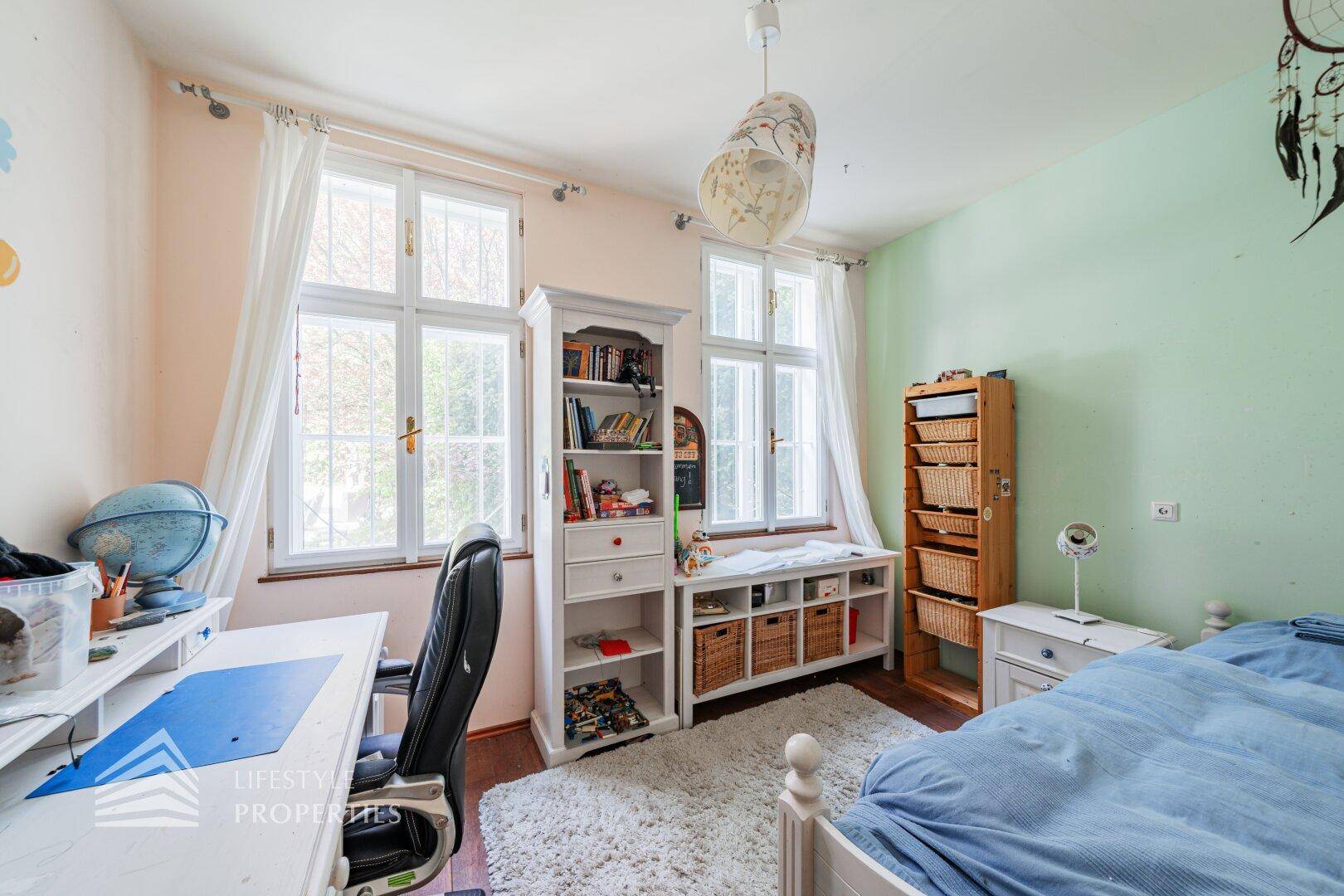 Kinderzimmer mit Schreibtisch, Holzboden und Blick ins Grüne.