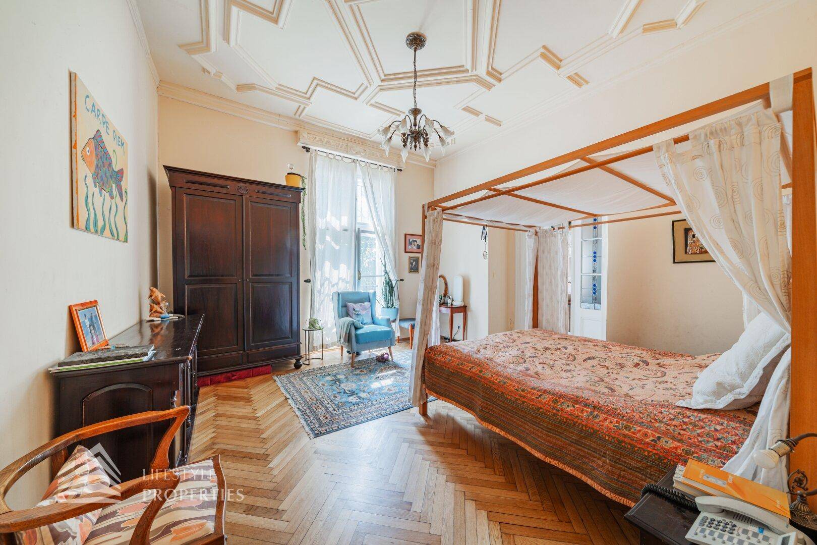 Elegantes Schlafzimmer mit Himmelbett, dunklem Holzschrank und Fischgrätparkett.