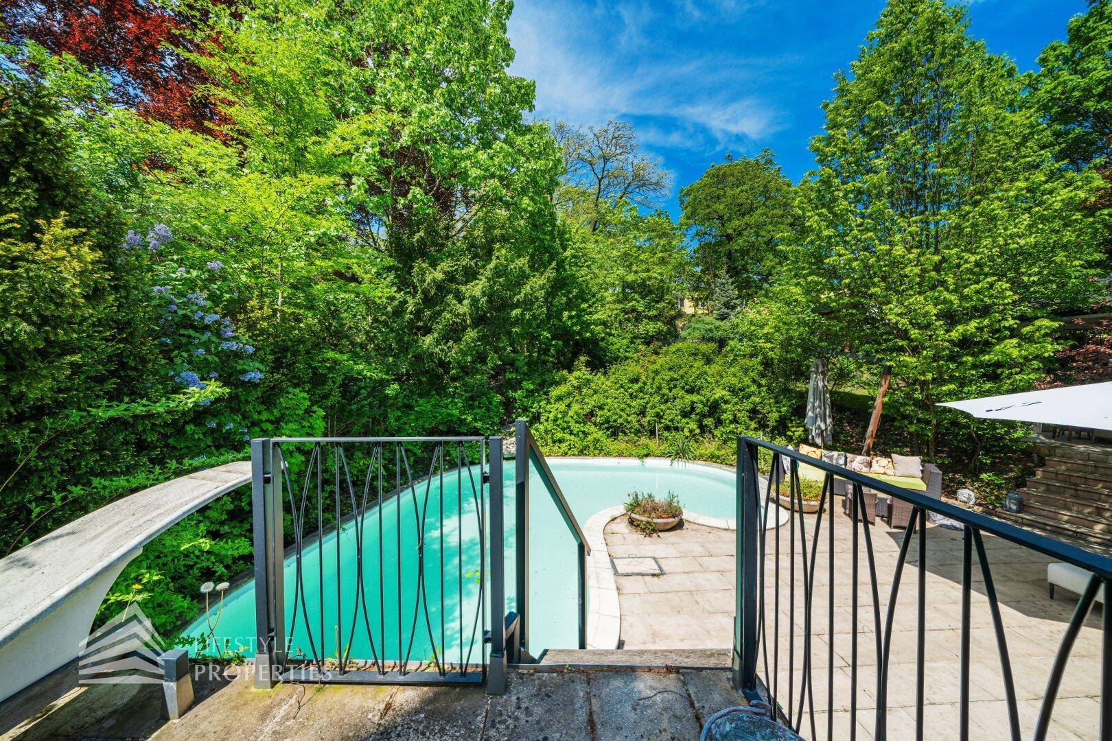 Blick auf den Poolbereich im Garten, umgeben von üppigem Grün und mit Zugangstreppe.