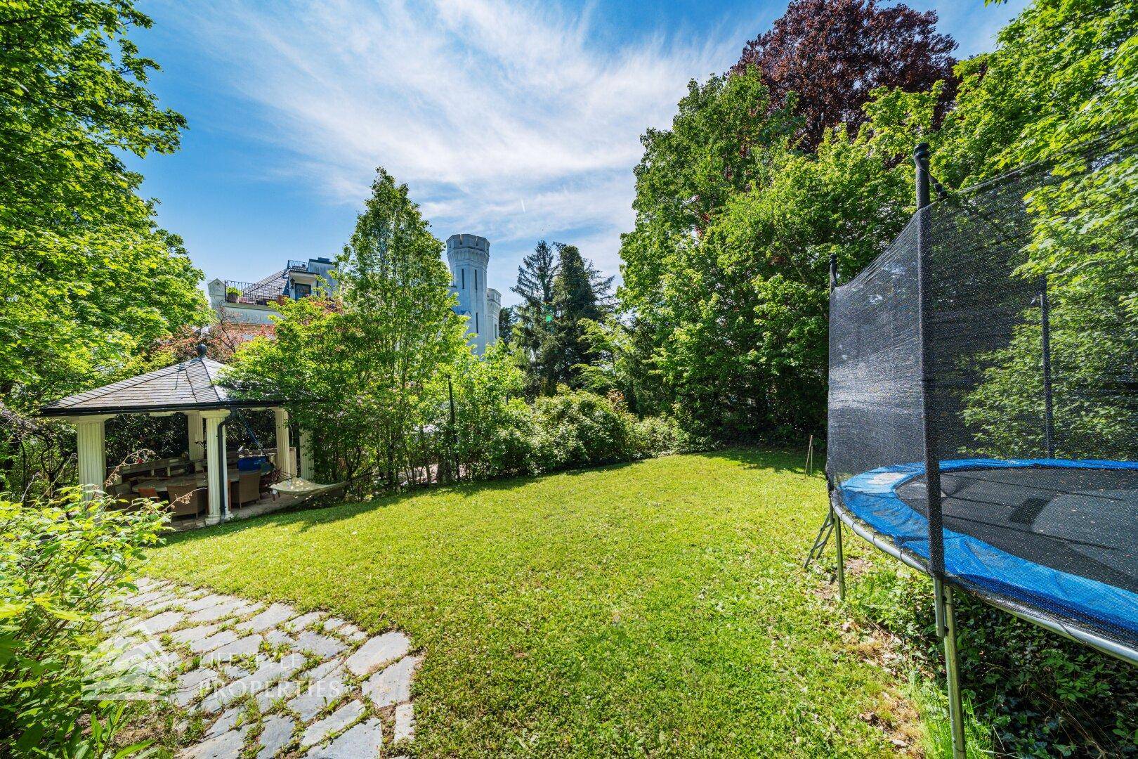 Großer Rasengarten mit Trampolin und einem Pavillon, umgeben von Bäumen.