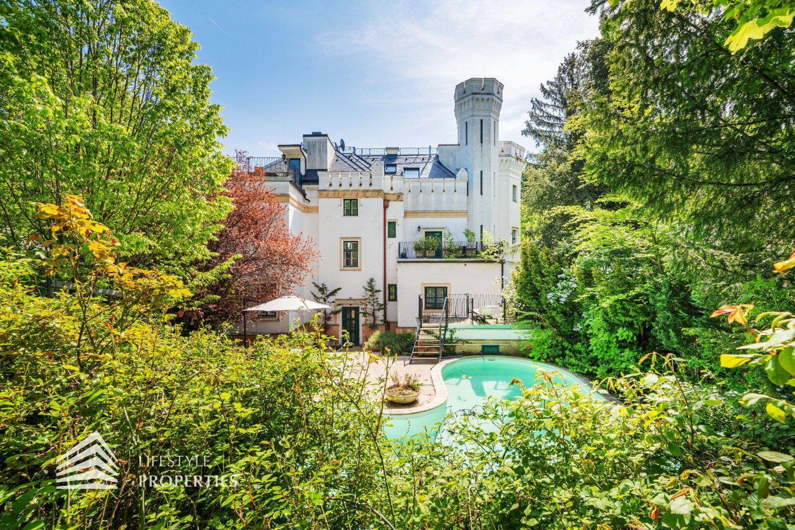 Beeindruckende Villa mit historischem Turm, umgeben von einem weitläufigen Garten mit Pool.