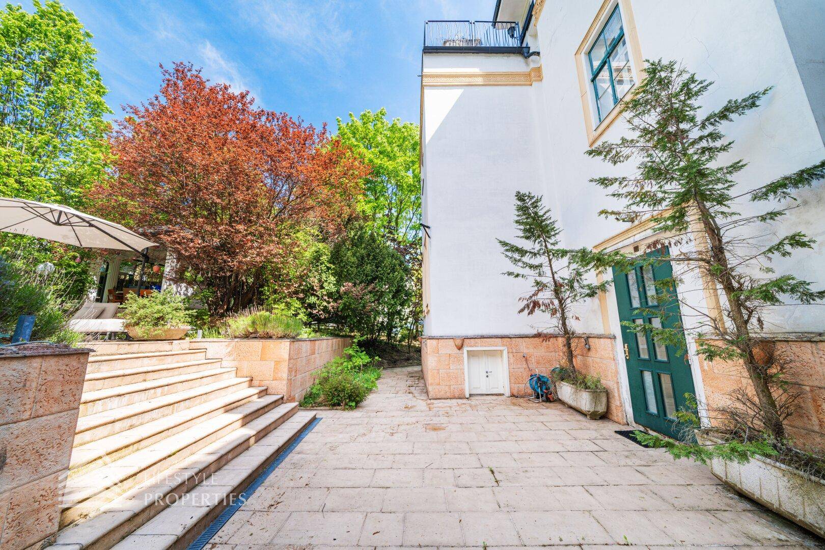 Seitenansicht des historischen Gebäudes mit Steintreppe und gepflastertem Weg, umgeben von Bäumen.