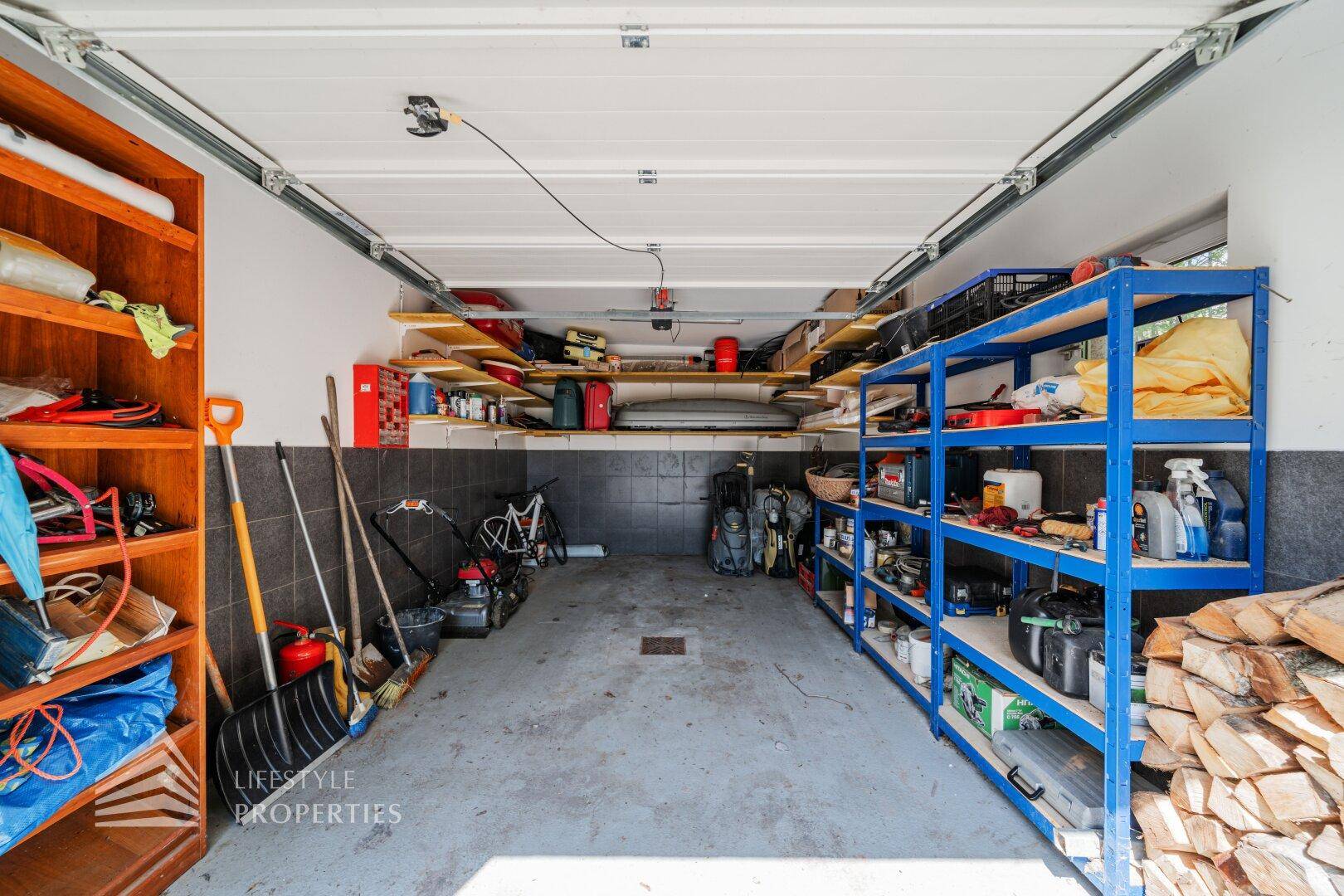 Geräumige Garage mit Regalen, Werkzeugen und Brennholz, ideal als Abstellraum.