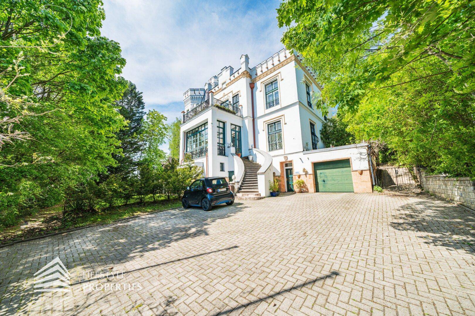 Vorderansicht des schlossähnlichen Gebäudes mit gepflasterter Auffahrt und integrierter Garage.