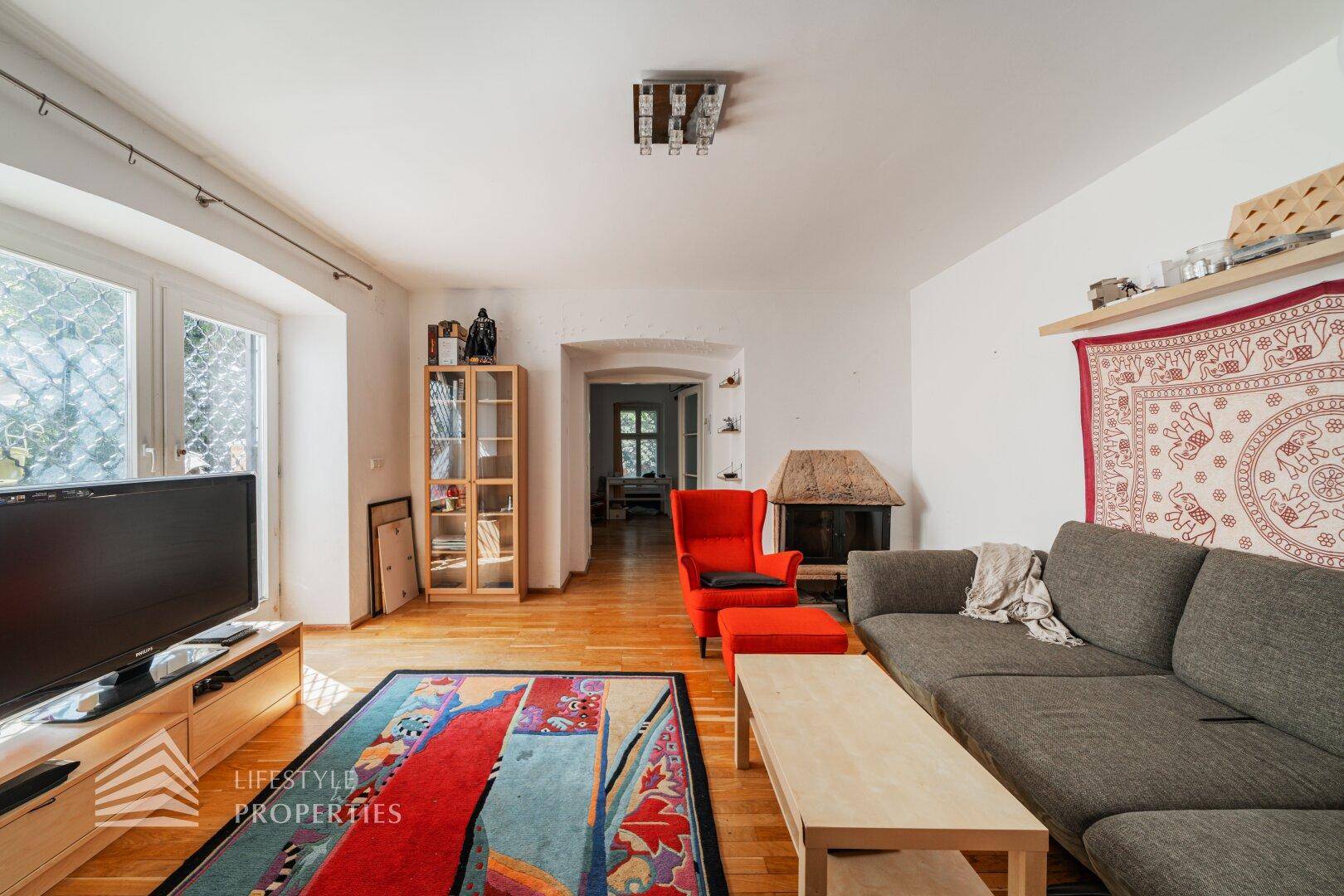 Gemütliches Wohnzimmer mit grauem Sofa, rotem Sessel und Holzboden, mit einem kleinen Kamin.