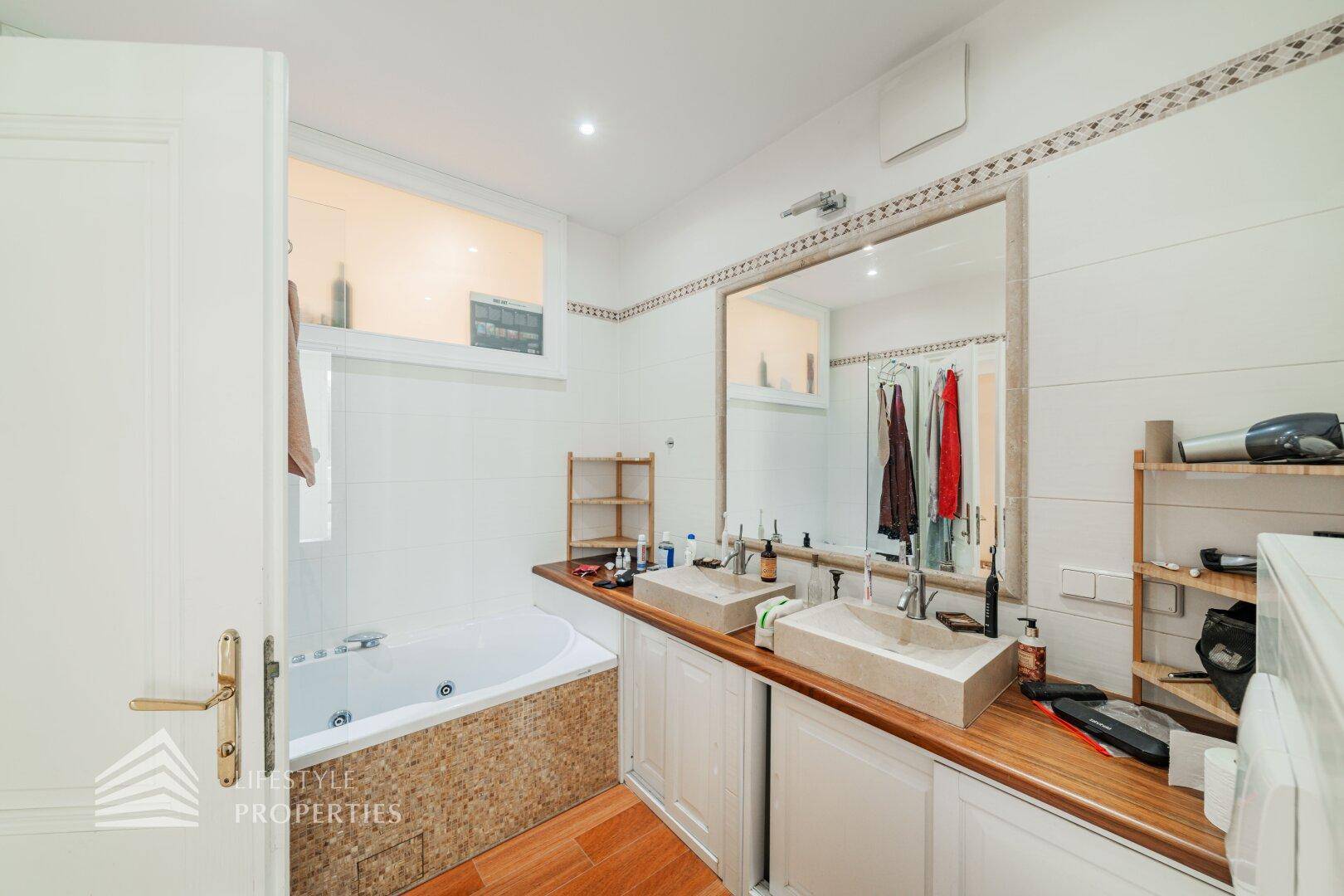 Helles Badezimmer mit Doppelwaschbecken, Badewanne und Holzarbeitsplatte.