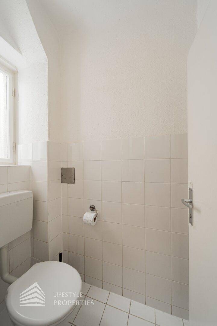 Separates WC mit Toilette, Fenster und weißen Wandfliesen.