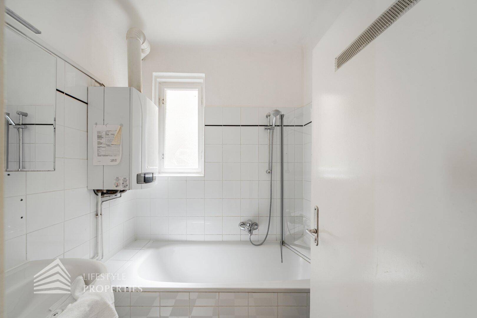 Badezimmer mit Badewanne, Duschvorrichtung und Fenster für Belüftung.