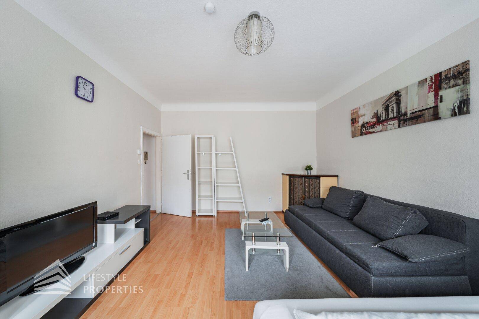 Wohnbereich mit Sofa, Fernseher, Couchtisch und Zugang zur Eingangstür.