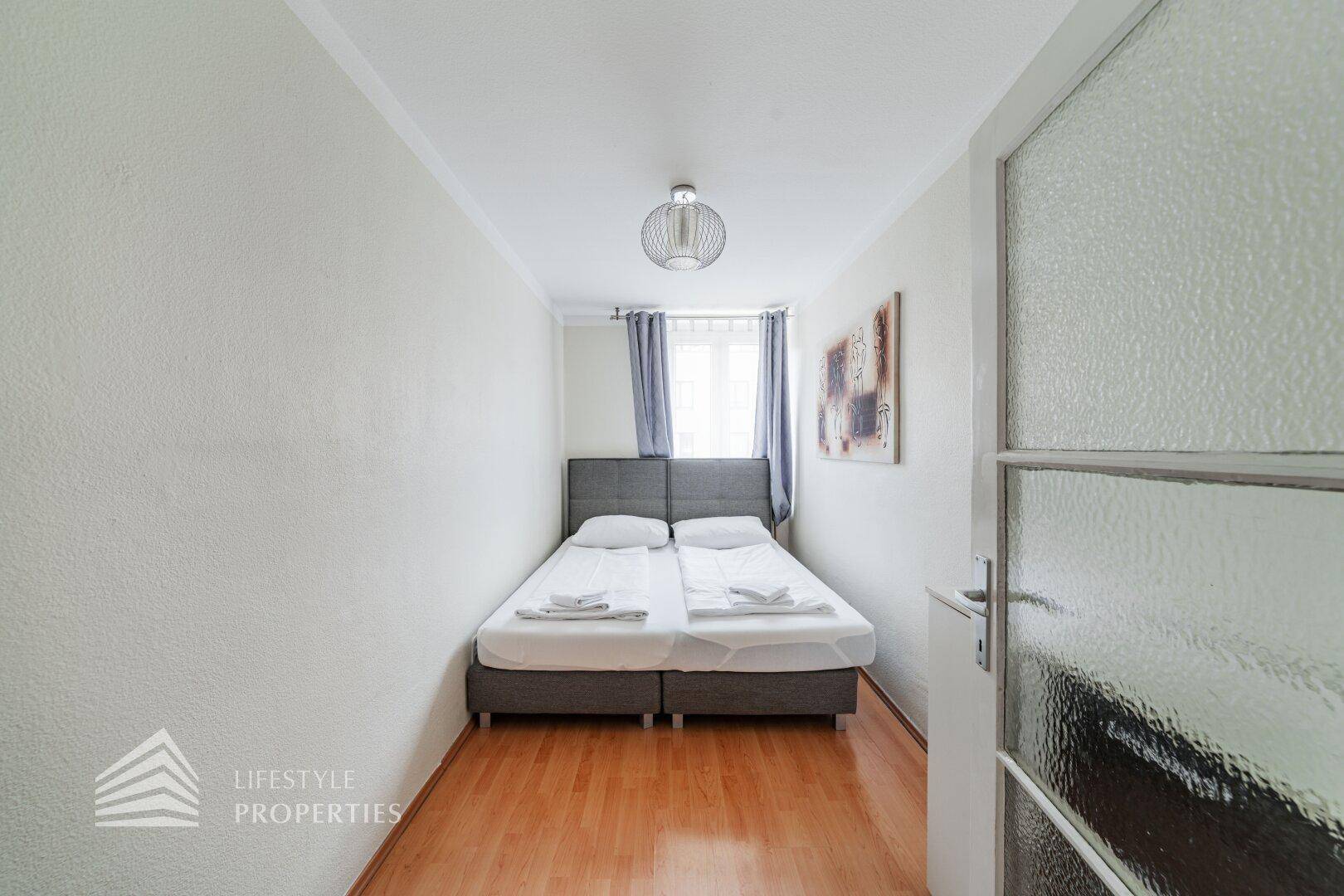 Schlafzimmer mit Doppelbett, hellem Holzfußboden und Fenster für natürliches Licht.