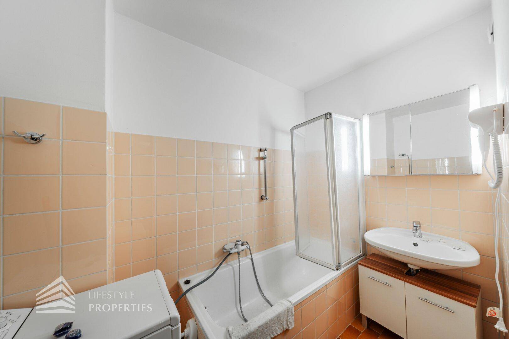 Badezimmer mit Badewanne, Duschabtrennung, Waschbecken und hellen Fliesen.