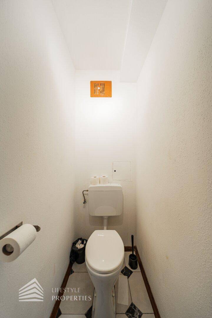 Kleines separates WC mit weißer Toilette und Abluftventilator.
