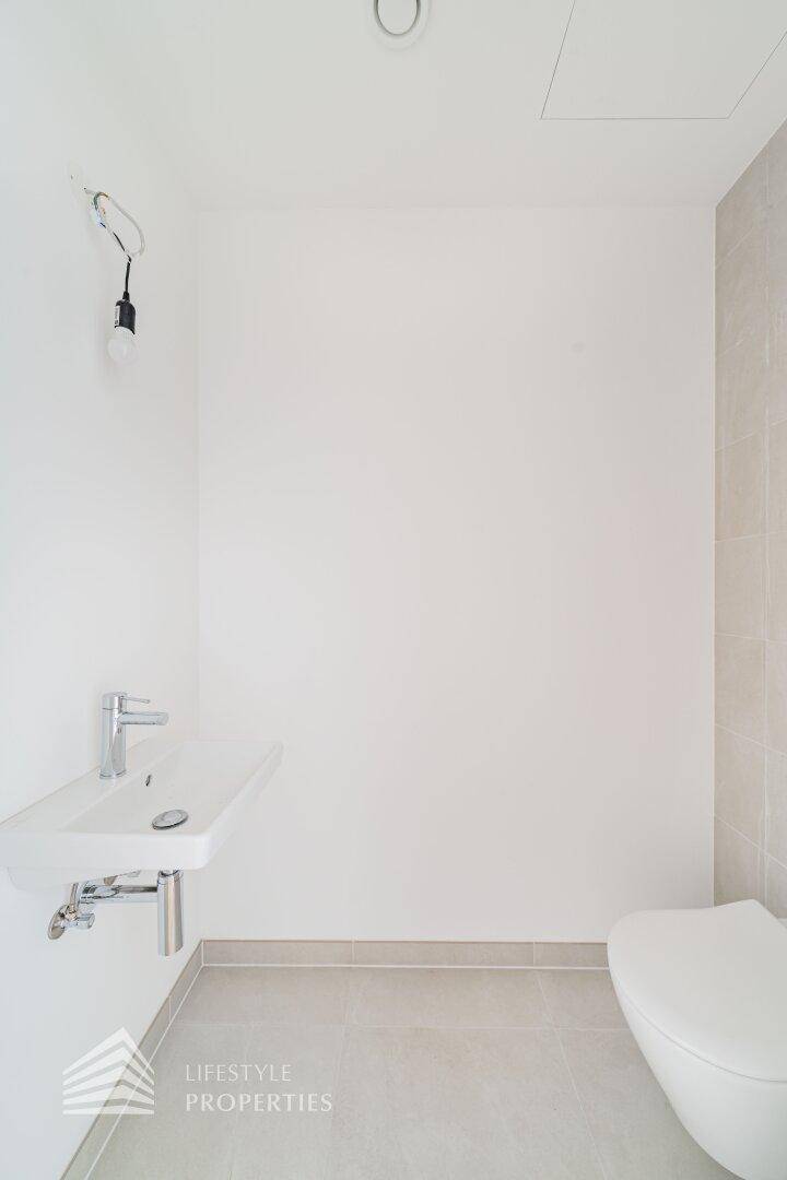 Modernes Gäste-WC mit wandhängendem WC und kleinem Waschbecken, hell gefliest.