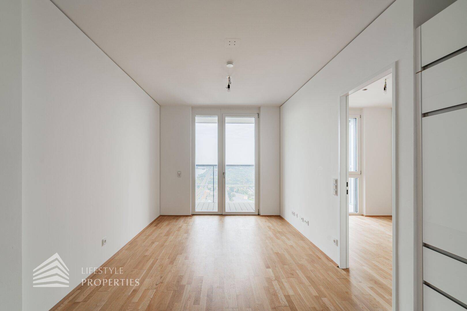 Geräumiges, helles Zimmer mit Holzboden und Zugang zu einem Balkon, ideal für Wohnzwecke.