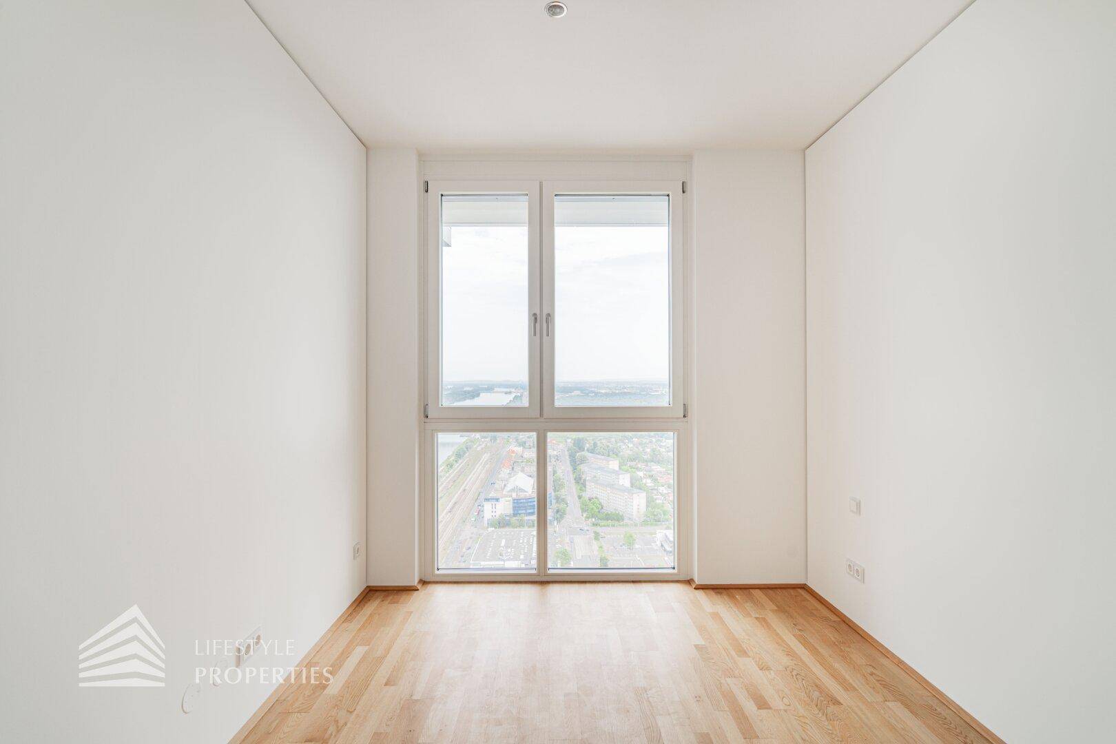 Helles Zimmer mit großem Fenster, Holzboden und weitem Blick über die Umgebung.
