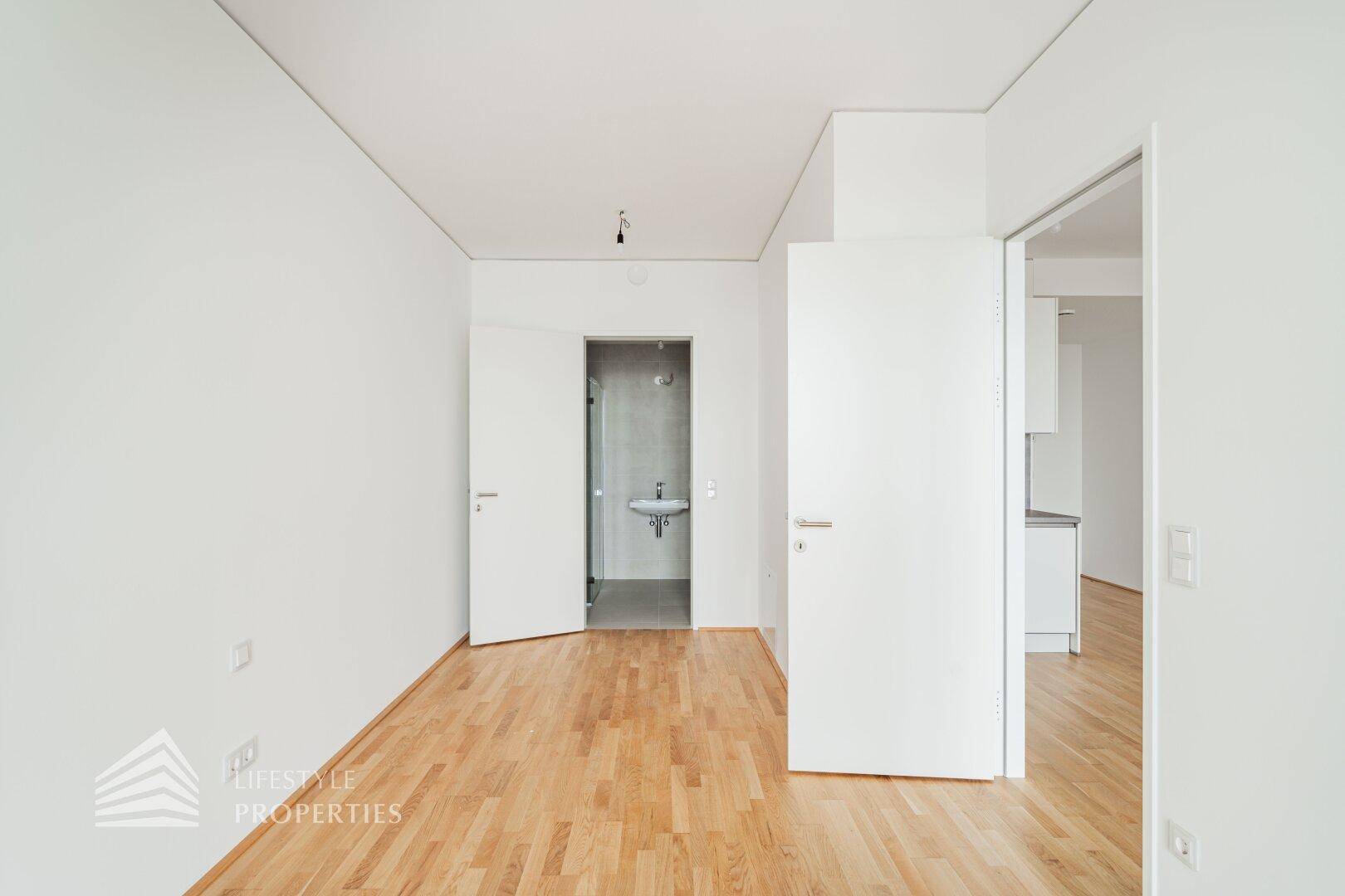 Helles Zimmer mit Holzboden und Zugang zu einem modernen Badezimmer.