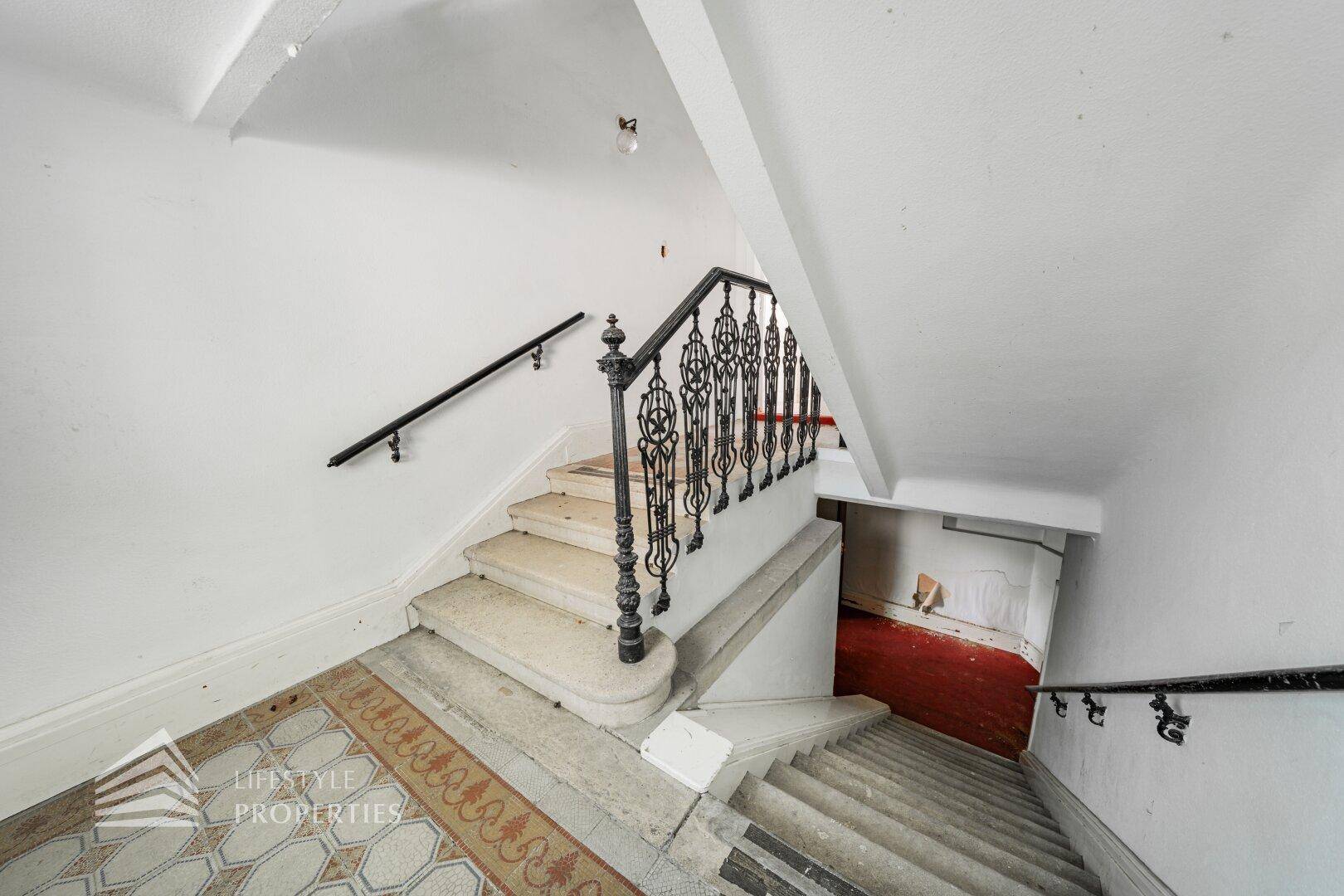 Historisches Treppenhaus mit kunstvollem schmiedeeisernem Geländer und Steinstufen.