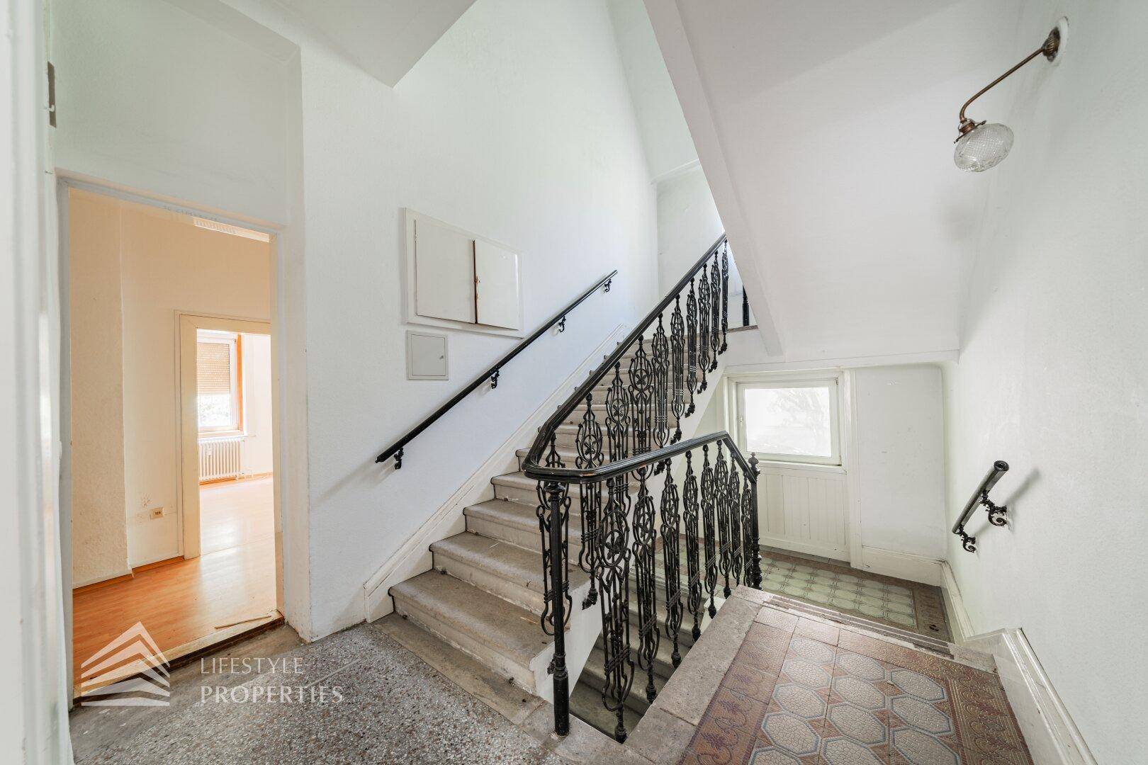 Elegantes Treppenhaus mit geschwungenem schmiedeeisernem Geländer und Tageslicht.