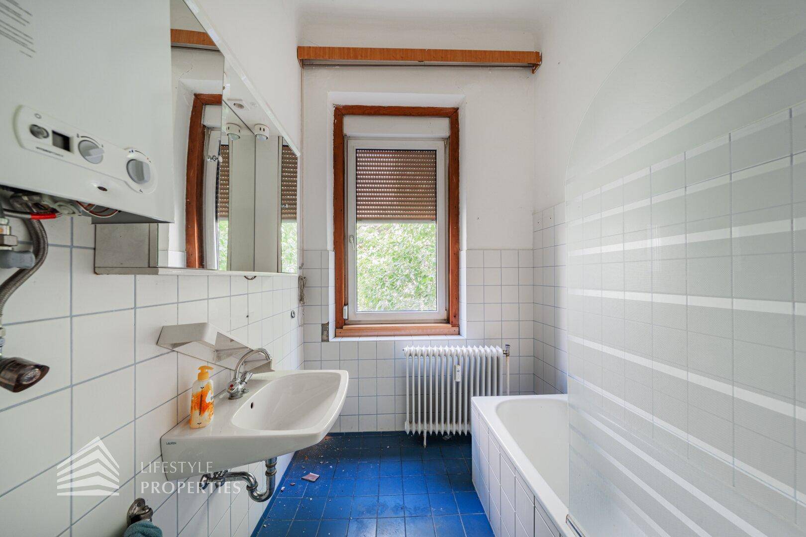 Badezimmer mit Badewanne, Waschbecken und Fenster, ausgestattet mit blauen Fliesen.