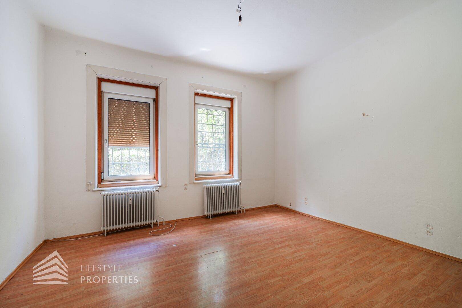 Zimmer mit Laminatboden und zwei Fenstern, ausgestattet mit Rollläden.