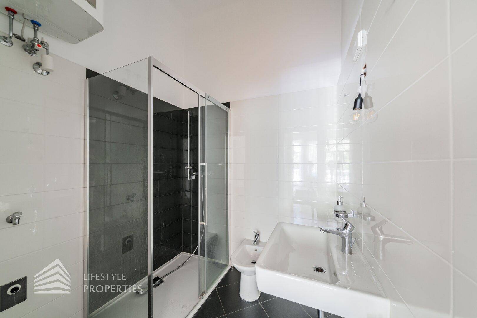 Modernisiertes Badezimmer mit Duschkabine, Waschbecken und Bidet in Weiß und Schwarz.