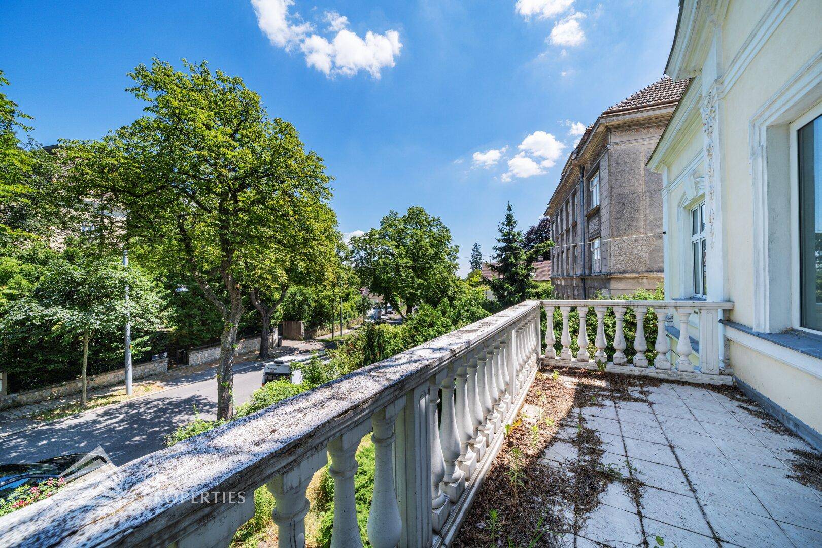 Geräumiger Balkon mit Balustrade und Blick auf die von Bäumen gesäumte Straße.
