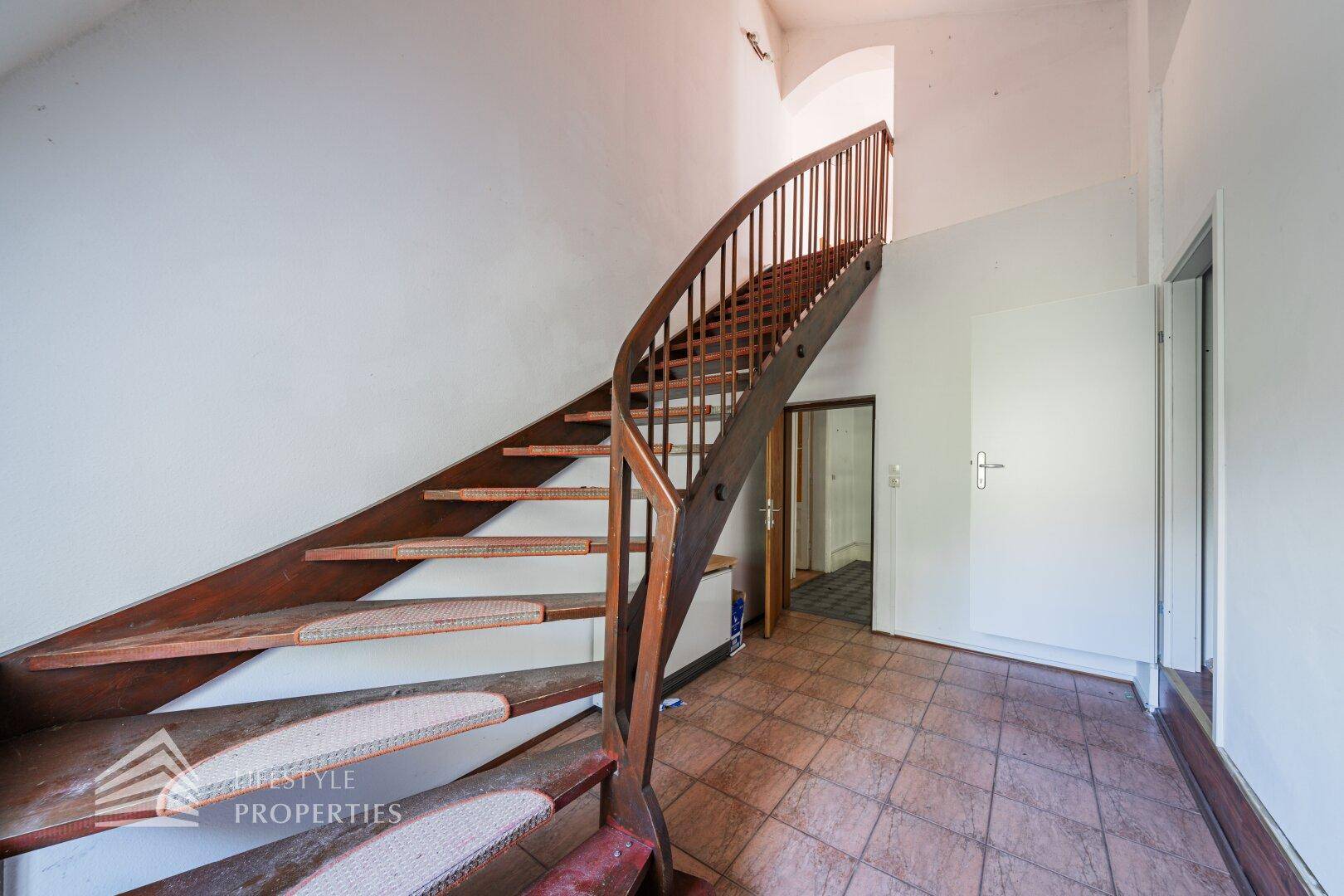Geschwungene Holztreppe mit Teppichstufen, die in das obere Stockwerk führt.
