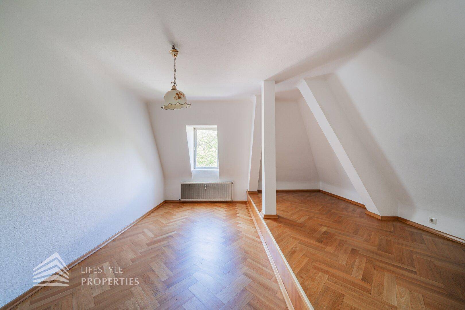 Helles Dachzimmer mit Parkettboden, Dachfenster und schrägen Wänden.
