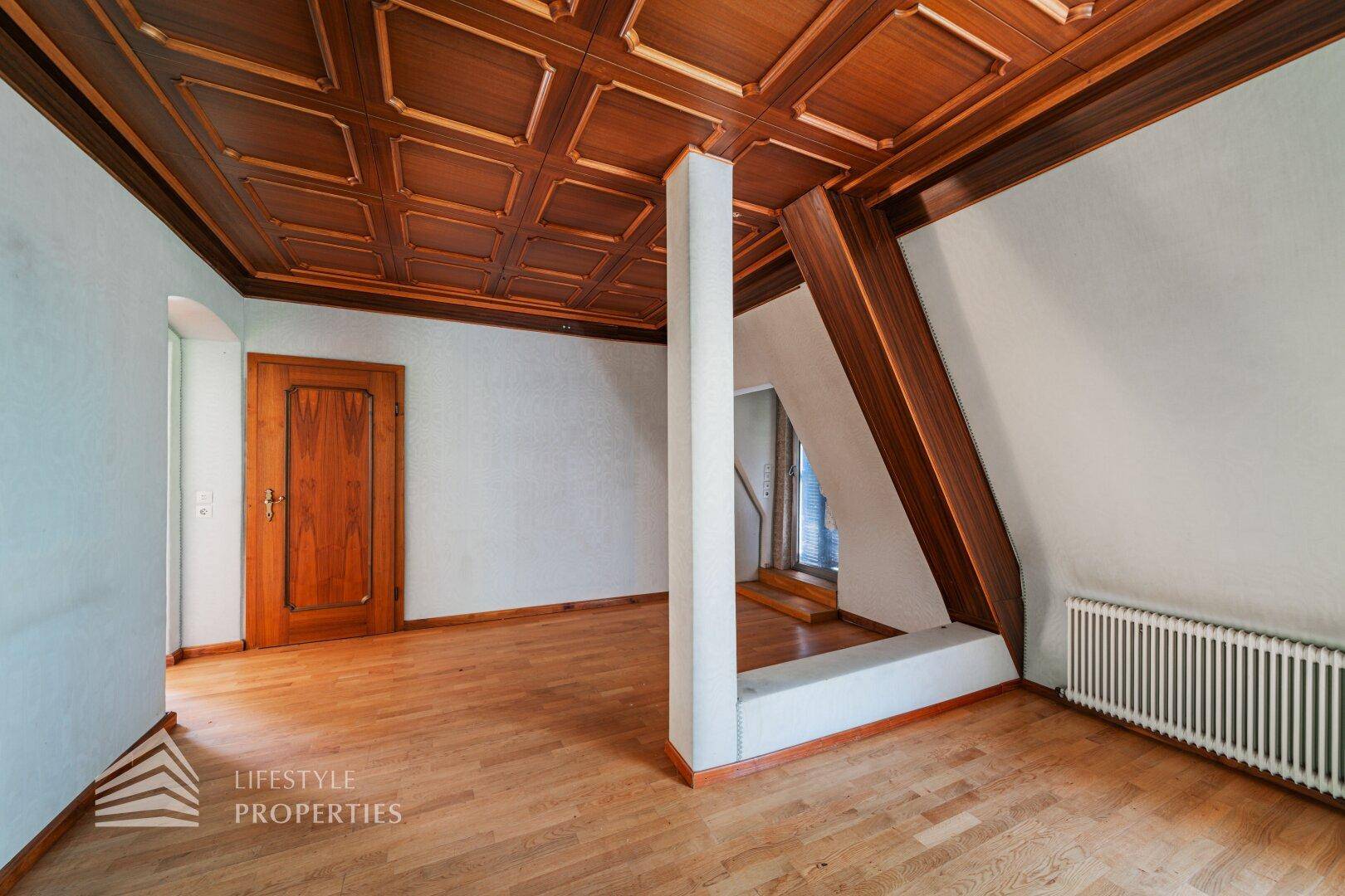 Teil des Wohnbereichs mit Holzkassettendecke und Parkettboden, offene Gestaltung.