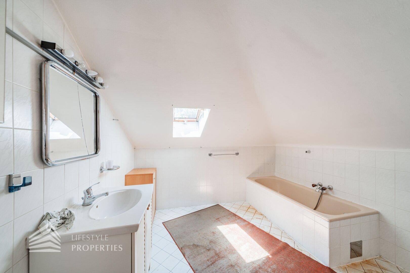 Dachbad mit Badewanne, Waschbecken und Dachfenster, in hellem Design.