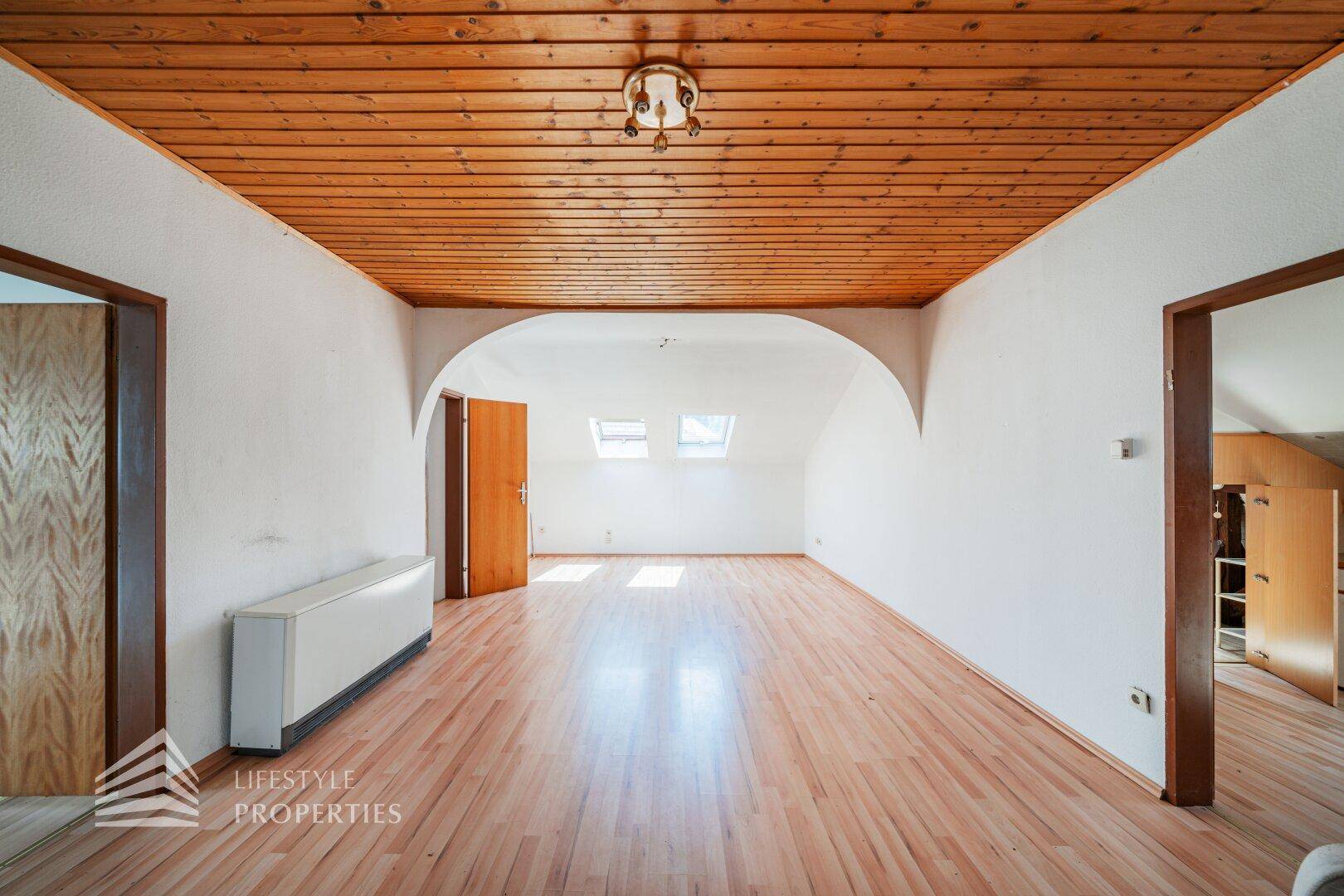 Geräumiges Dachzimmer mit Holzdecke, Laminatboden und zwei Dachfenstern.