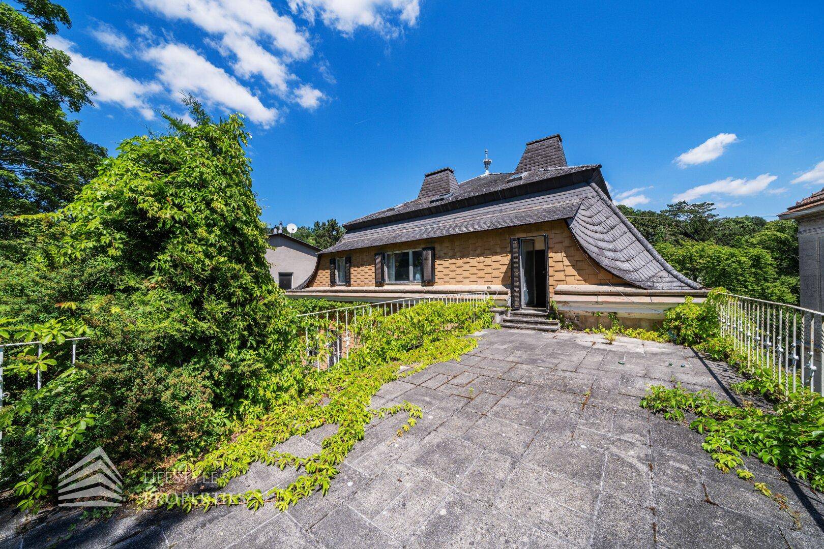 Rückseite des Hauses mit großer gepflasterter Terrasse und markantem Dach.