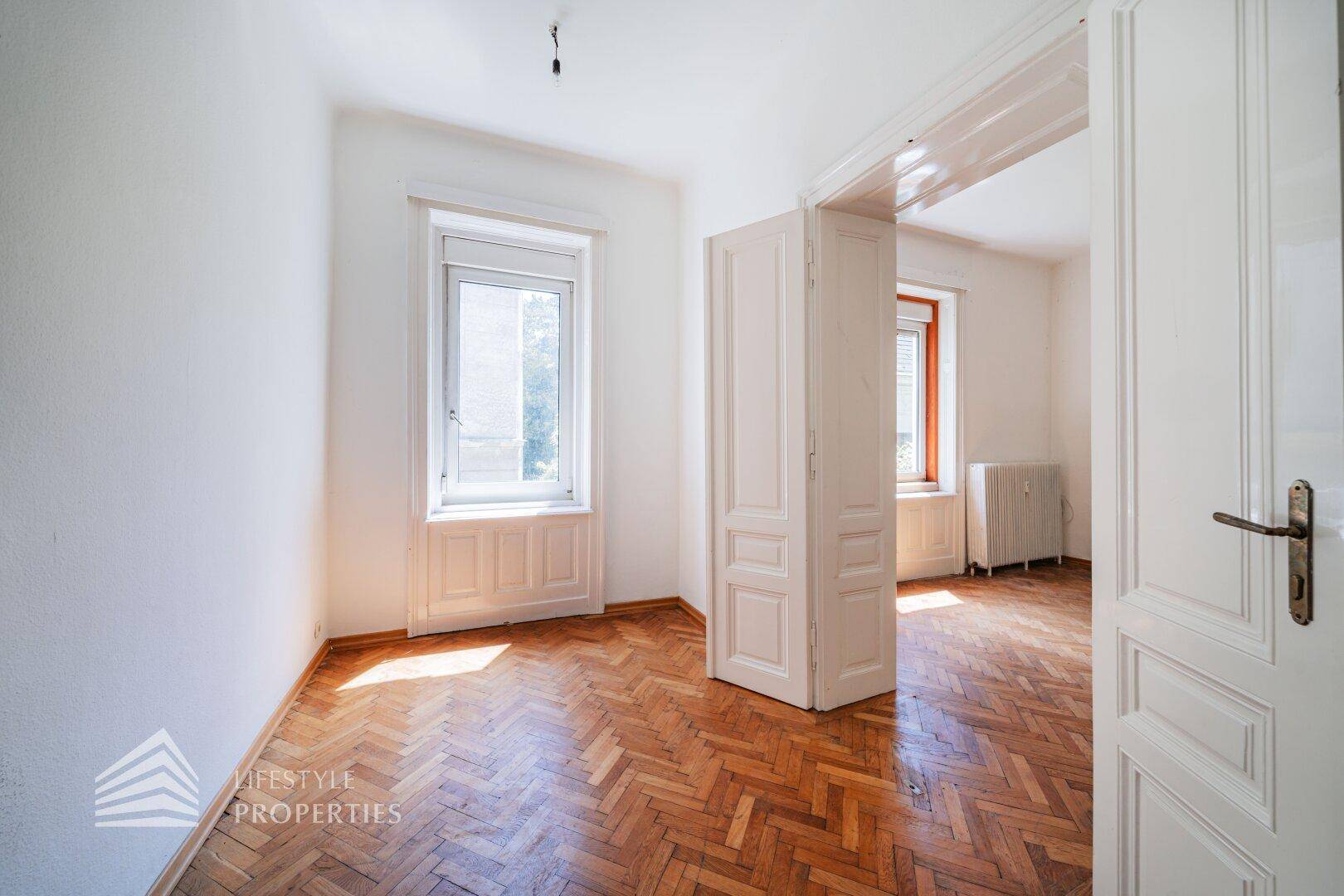 Helles Zimmer mit Fischgrätparkett und hohen Fenstern, ideal für individuelle Gestaltung.