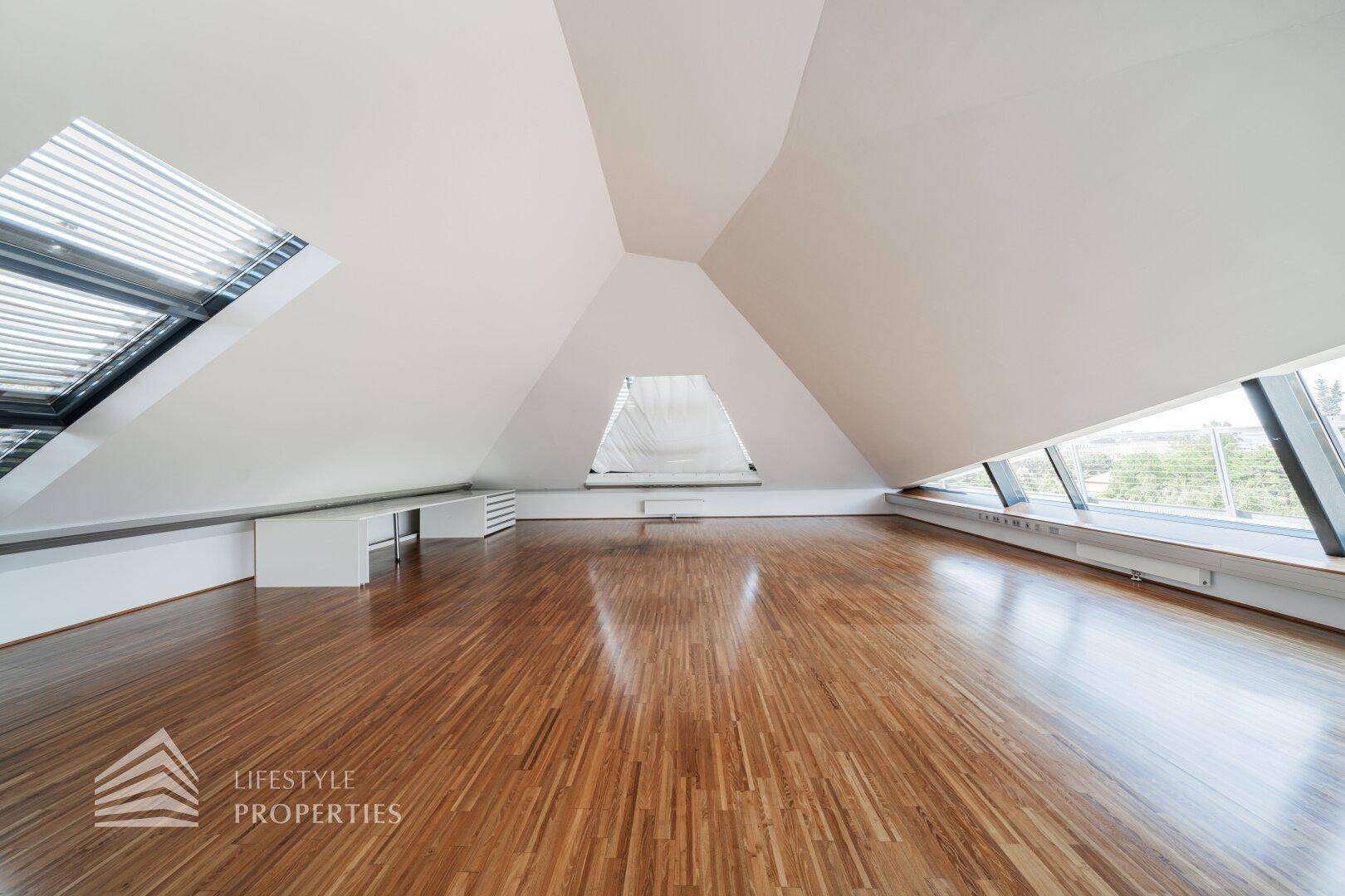 Weitläufiger Dachgeschossraum mit markanten schrägen Decken und großen Fenstern für viel Licht.