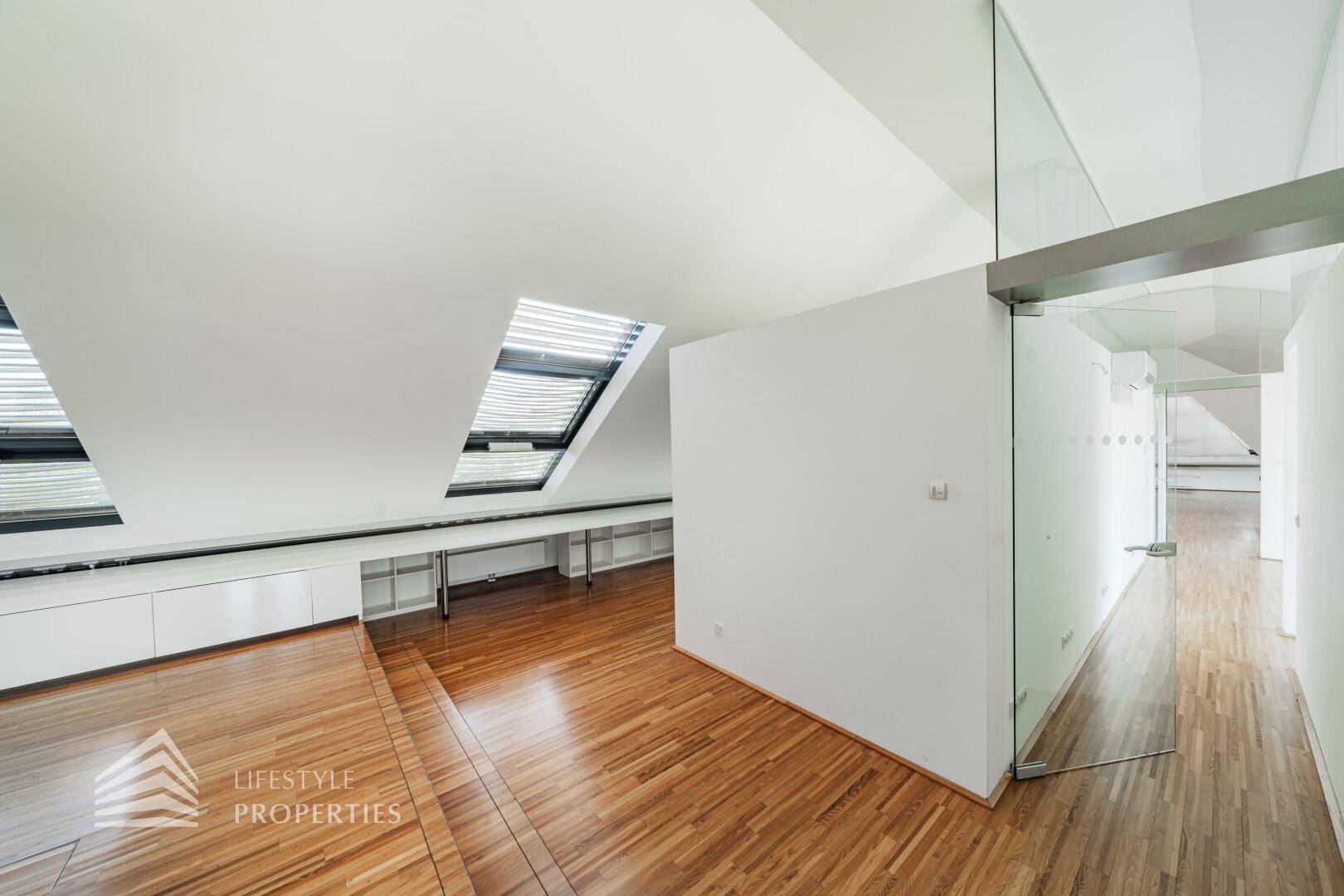 Dachgeschosswohnung mit Holzboden, Dachfenstern und einer modernen Glastür zum Flur.